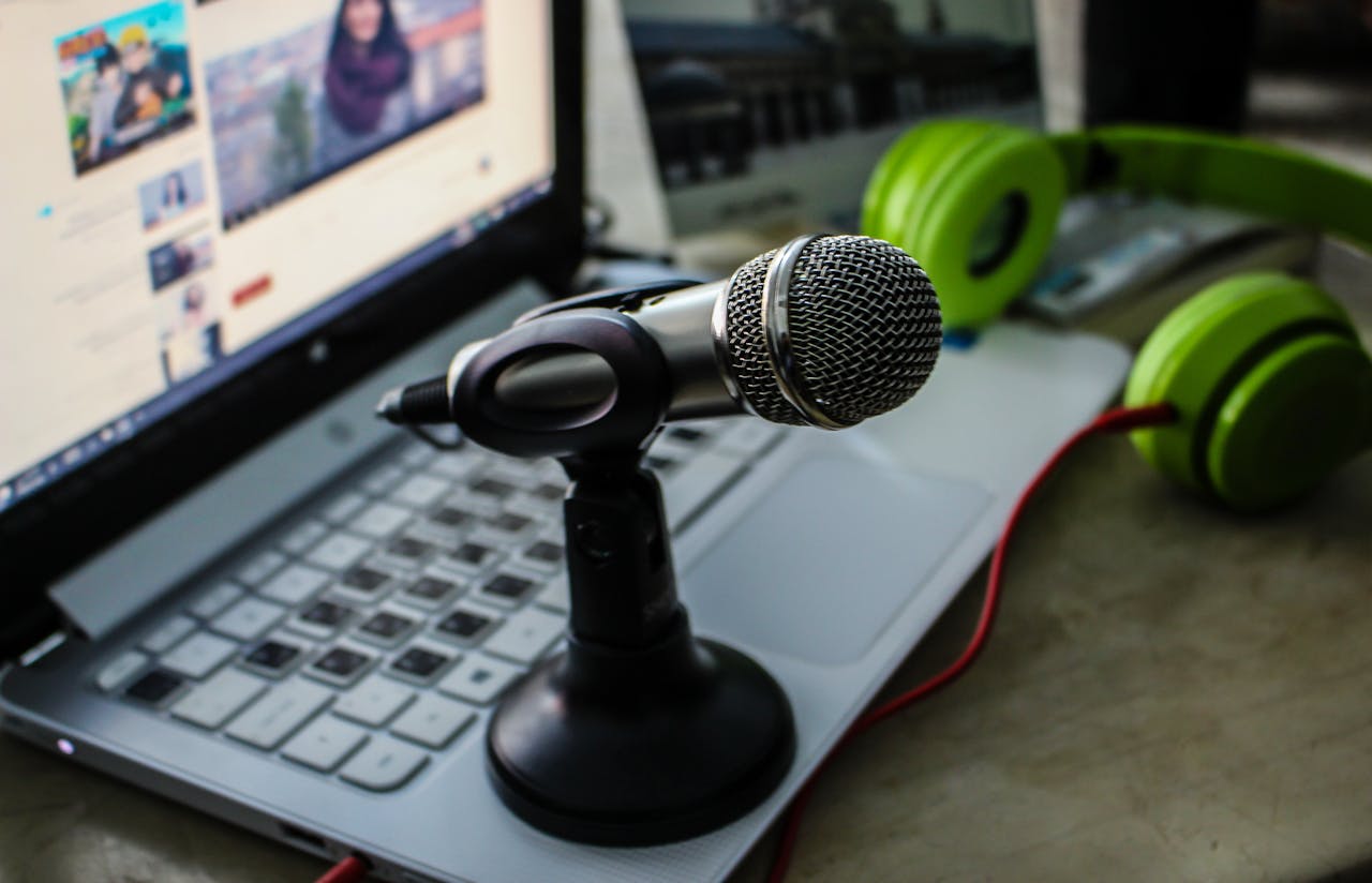 services-02 Close-up of a podcasting setup with a microphone, laptop, and green headphones.