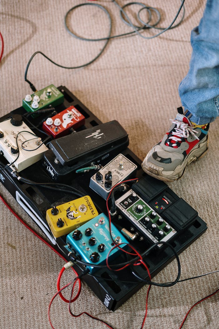 journey Close-up of a musician's foot on a pedalboard with various colorful guitar effects pedals in a home studio.