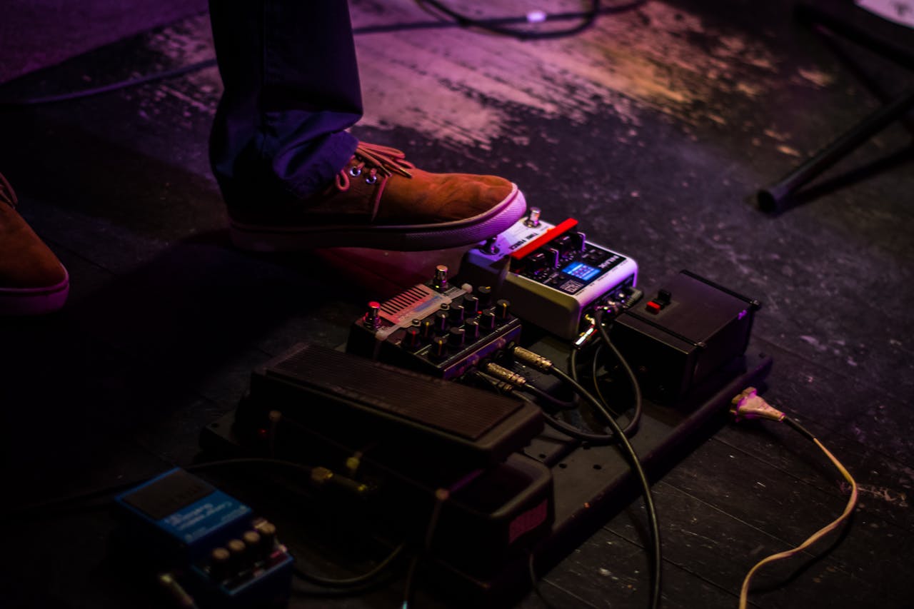 who-we-are Close-up of a musician's foot operating a guitar pedal board during a live performance.
